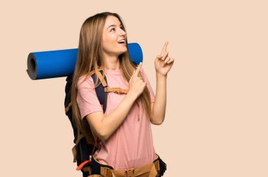 Genç sırt çantalı kadın işaret parmağıyla işaret ederek izole edilmiş sarı arka plana bakıyor.