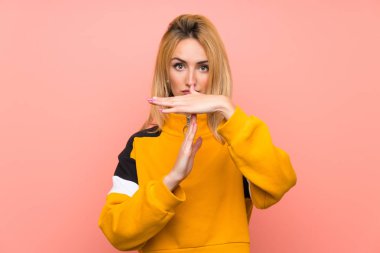 Soyutlanmış pembe arka planda genç sarışın bir kadın zaman geçirme hareketi yapıyor.