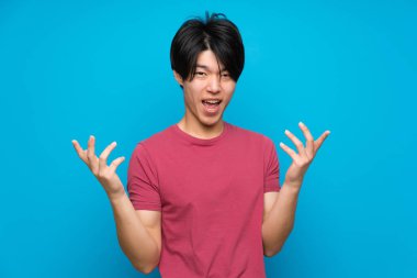 Izole mavi duvar üzerinde kırmızı gömlek li Asyalı adam mutsuz ve bir şey ile sinirli