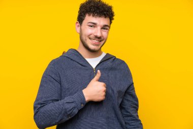 Izole sarı duvar üzerinde genç adam jest kadar bir başparmak veren