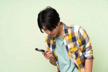 Bir büyüteç tutan izole yeşil duvar üzerinde Asyalı adam