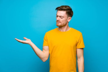 Şüphelerle copyspace tutan mavi duvar üzerinde Redhead adam