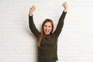 Beyaz tuğla duvarın üzerinde zaferi kutlayan genç bir kadın.