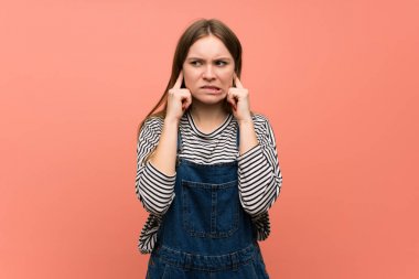 Pembe duvarın üzerinde elleri kulakları olan genç bir kadın. Hayal kırıklığına uğramış ifade