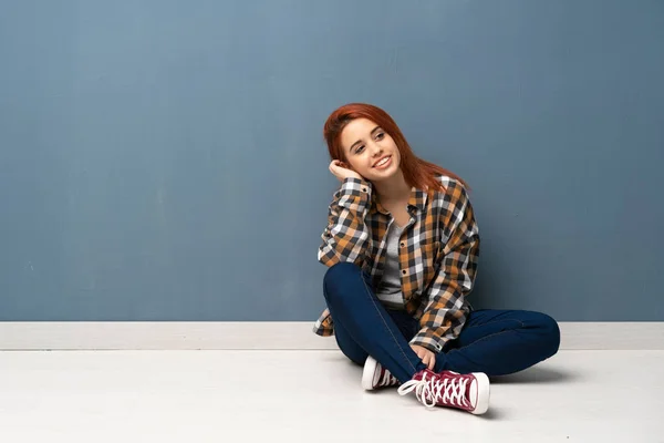 Young redhead woman sitting on floor thinking an idea while scratching head