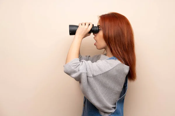 隔離された背景との距離で双眼鏡で見て若い赤毛の女性 — ストック写真