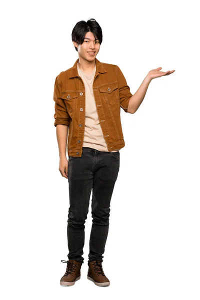 孤立した白い背景の上に広告を挿入するために手のひらにコピースペースの架空を保持する茶色のジャケットを持つアジア人男性のフルレングスショット — ストック写真