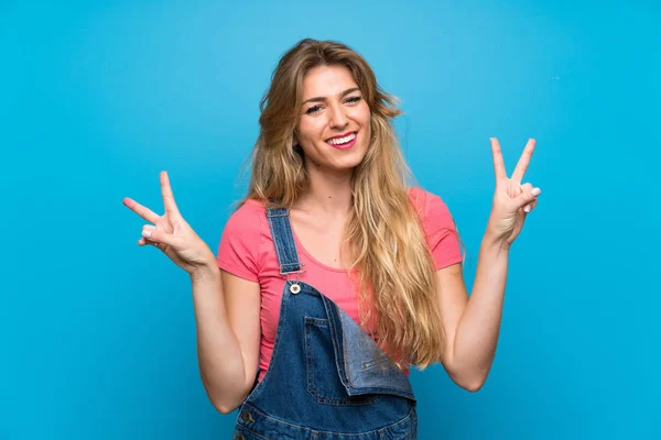 Young Blonde Woman Overalls Isolated Blue Wall Showing Victory Sign — Stock Photo, Image