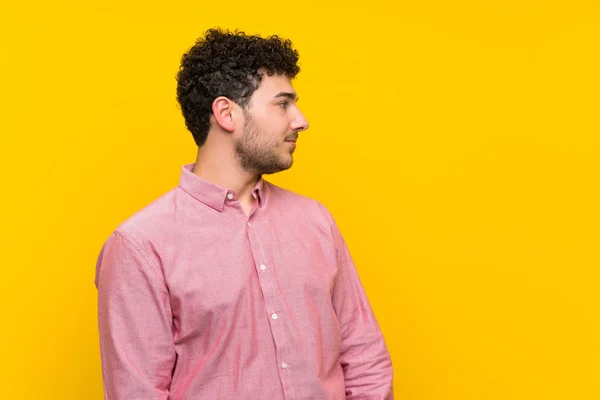 Man Met Krullend Haar Geïsoleerde Gele Muur Staande Zoek Naar — Stockfoto