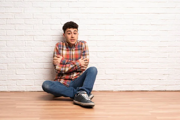 Young man sitting on the floor freezing