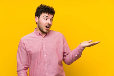 İzole sarı duvar üzerinde kıvırcık saçlı adam avuç içi üzerinde copyspace hayali tutan