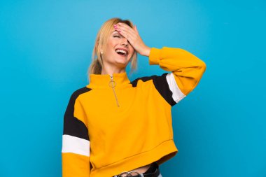 Soyutlanmış mavi arka planda genç sarışın kadın gülüyor.