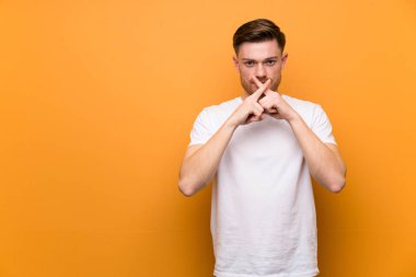 Kahverengi duvarın üzerinde sessizlik jesti gösteren kızıl saçlı adam