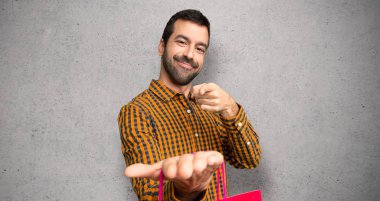 Dokuma duvar üzerine bir reklam eklemek için palmiye üzerinde boşaltmak hayali tutan alışveriş çantaları ile adam