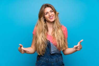 Genç sarışın kadın mavi duvardan aşağı sarkık, gururlu ve kendini beğenmiş.