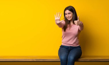 Masada oturan genç kadın parmaklarıyla altıya kadar sayıyor.