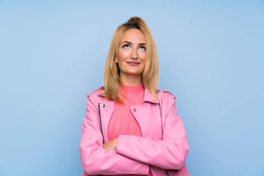 Pembe ceketli genç sarışın kadın izole edilmiş mavi arka planda gülümserken yukarı bakıyor.