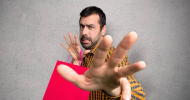 Alışveriş çantaları ile Adam biraz gergin ve dokulu duvar üzerinde ön elleri germe korkuyor