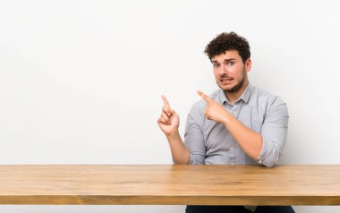 Masası olan genç adam korkmuş ve kenarı işaret ediyor.