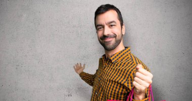 Alışveriş poşetleri ile Adam geri işaret ve dokulu duvar üzerinde bir ürün sunan