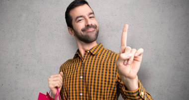 Dokulu duvar üzerinde en iyi işareti gösteren ve bir parmak kaldırma alışveriş çantaları ile Adam