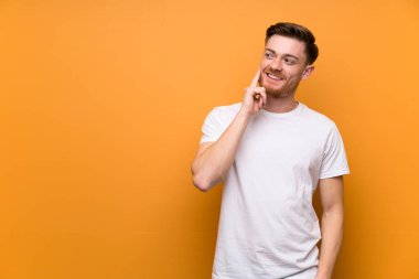 Kırmızı saçlı adam kahverengi duvar üzerinde yukarı bakarken bir fikir düşünüyor