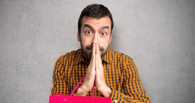 Alışveriş poşeti olan adam avuç içini bir arada tutar. Kişi dokulu duvar üzerinde bir şey ister