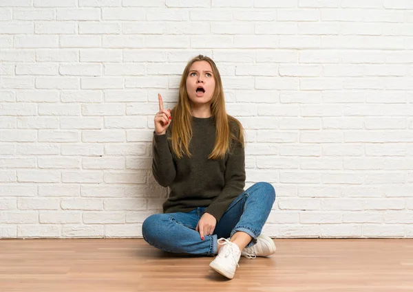 Junge Frau Sitzt Auf Dem Boden Und Zeigt Nach Oben — Stockfoto