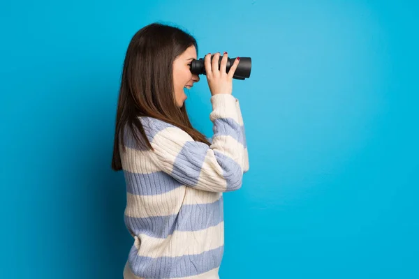 年轻女子越过蓝色的墙壁 用双筒望远镜在远处看 — 图库照片