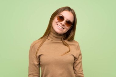 Boğazlı kazaklı, gözlüklü ve gülümseyen genç bir kadın.