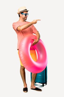 Onun yaz tatili yan işaret parmak şapka ve güneş gözlüğü ile Man Tam vücut ve izole arka plan üzerinde yanal pozisyonda bir ürün sunan