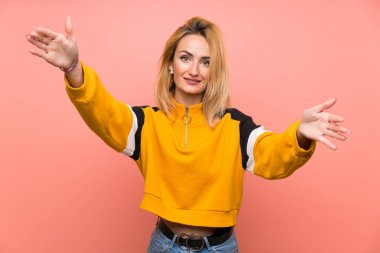 İzole edilmiş pembe arka planı olan genç sarışın kadın sunar ve davet eder.