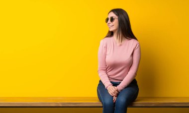 Genç bir kadın gözlükleriyle masada oturuyor ve gülümsüyor.