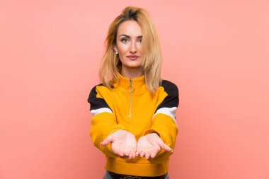 İzole edilmiş pembe arka planı olan genç sarışın kadın bir ilan vermek için avucunda hayali bir fotokopi makinesi tutuyor.