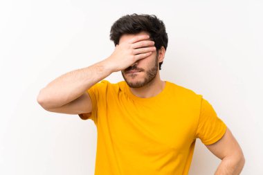 Elleriyle gözleri kaplayan izole beyaz duvar üzerinde Yakışıklı