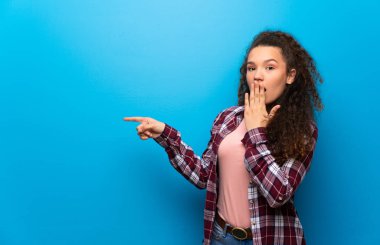 Mavi duvar üzerinde genç kız sürpriz bir yüz ile yan parmak işaret