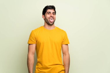 Genç adam pembe duvarın arkasında kameraya dil gösteriyor. Komik bir bakışı var.