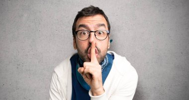 Gözlüklü bir işaret parmağını ağzına dokulu duvar'ın üstüne koyarak sessizlik jest gösteren yakışıklı adam