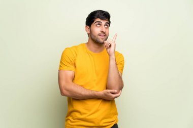 Genç adam pembe duvarın üzerinden harika bir fikir işaret ediyor ve yukarı bakıyor.