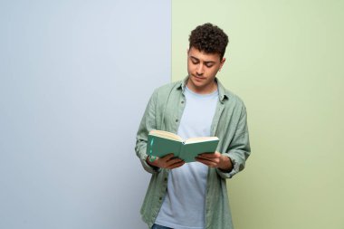 Genç adam bir kitap ve okuma zevk mavi ve yeşil arka plan üzerinde