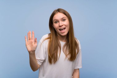 Mutlu ifade ile el ile Saluting mavi duvar üzerinde genç kadın