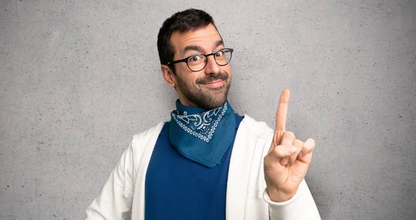 Handsome man with glasses showing and lifting a finger in sign of the best over textured wall