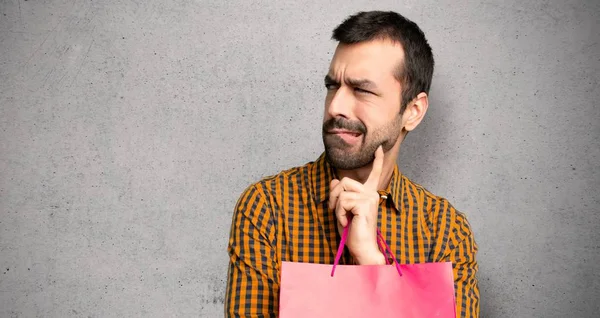 Man with shopping bags with confuse face expression while bites lip over textured wall