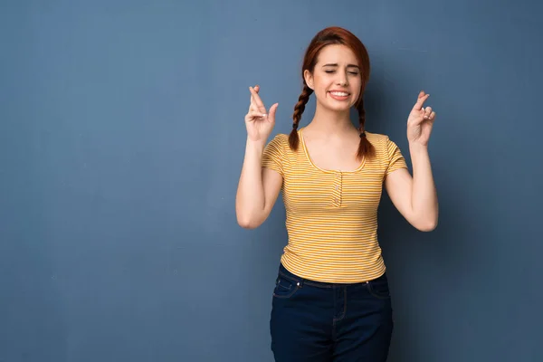 Young redhead woman over blue background with fingers crossing and wishing the best