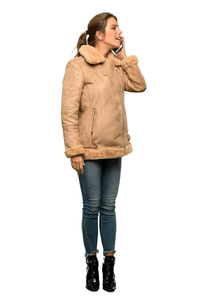 孤立した白い背景の上に携帯電話との会話を保つコートを着たブロンドの女性のフルレングスショット — ストック写真