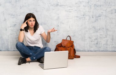 Öğrenci kadın kafasına parmak koyarak delilik jesti yaparak yerde oturan