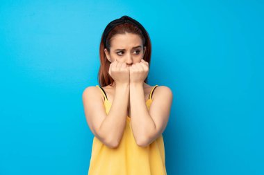 Mavi arka planda genç kızıl saçlı kadın gergin ve korkmuş, elleriyle suni teneffüs yapıyor.