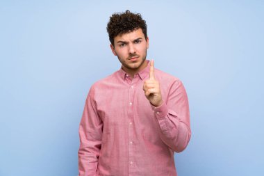 Izole mavi duvar üzerinde kıvırcık saçlı adam sinirli ve ön işaret