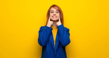 Trençkotlu genç kızıl saçlı kadın mutlu ve hoş bir ifadeyle gülümsüyor.