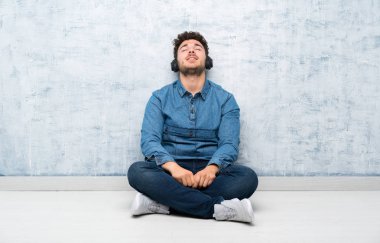 Yerde oturan genç adam kulaklıkla müzik dinliyor